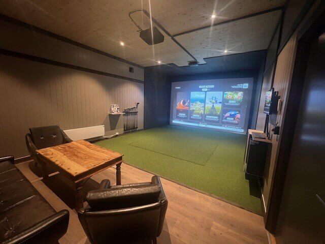 Indoor golfsimulator med storskjerm, kunstgress og sittegruppe i en moderne, stilfullt innredet stue.