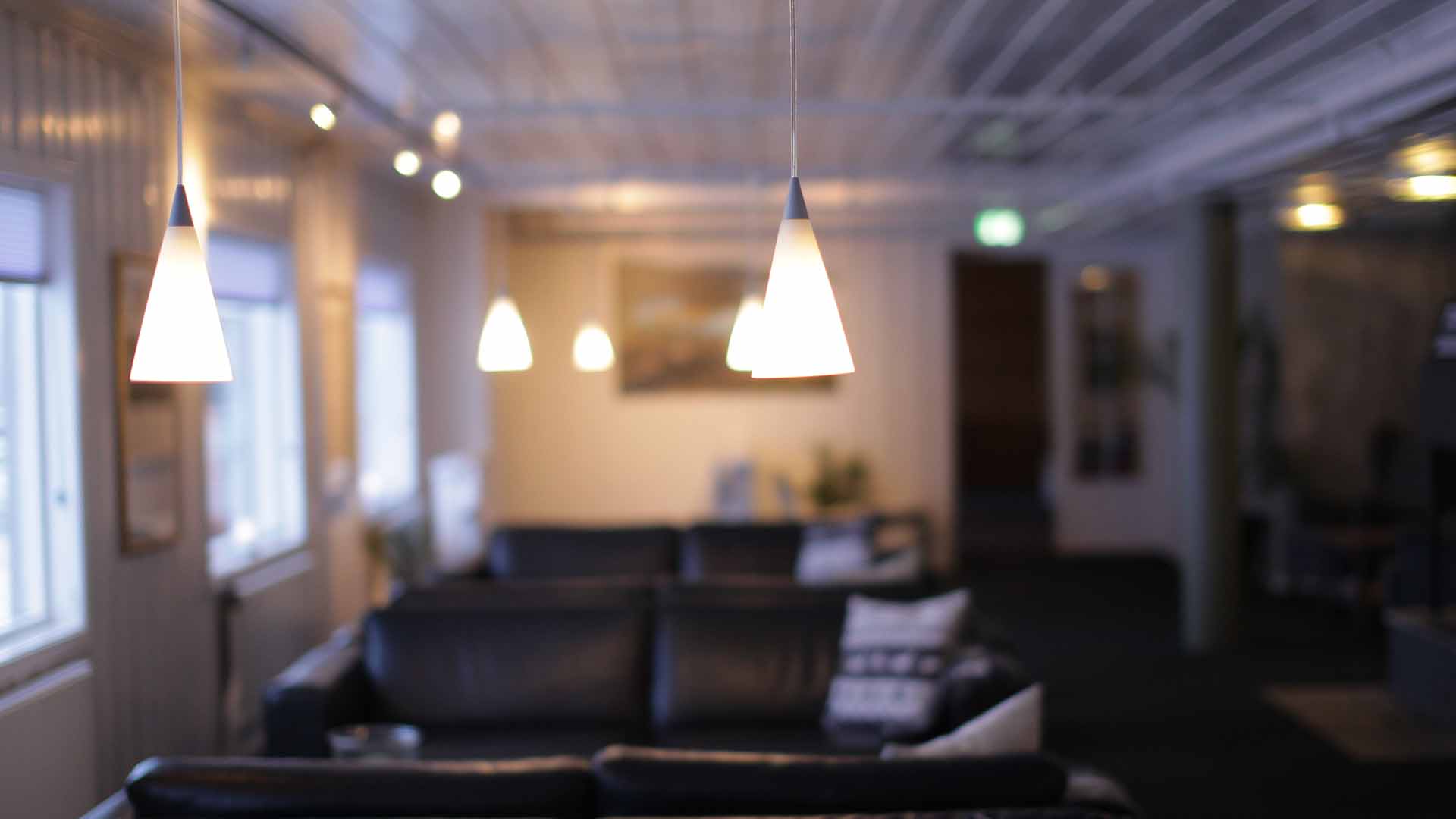 Moderne stue med hengende lamper, svarte sofaer og myk belysning for en koselig atmosfære.