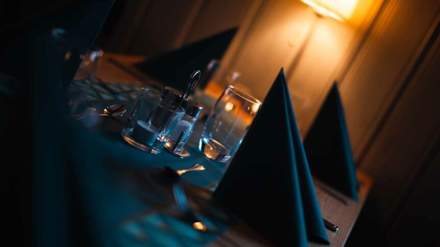 Romantisk bordsetting med tent lampe, glass og servise i dempet belysning.
