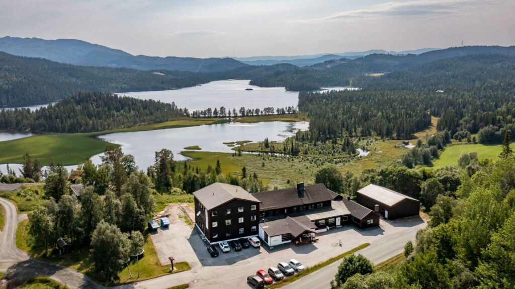 Flyfoto av norsk landskap med skog, innsjøer og bygninger, ideelt for naturopplevelser og rekreasjon.