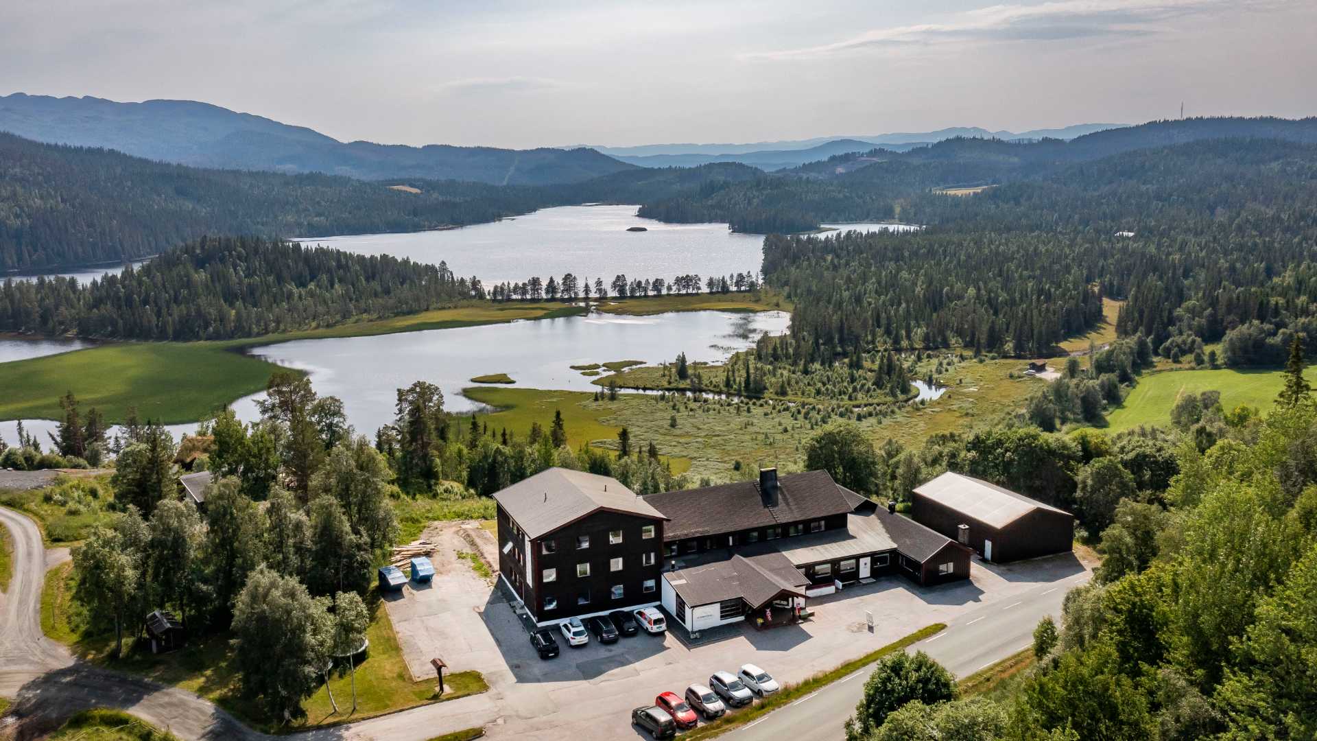 Flyfoto av norsk landskap med skog, innsjøer og bygninger, ideelt for naturopplevelser og rekreasjon.