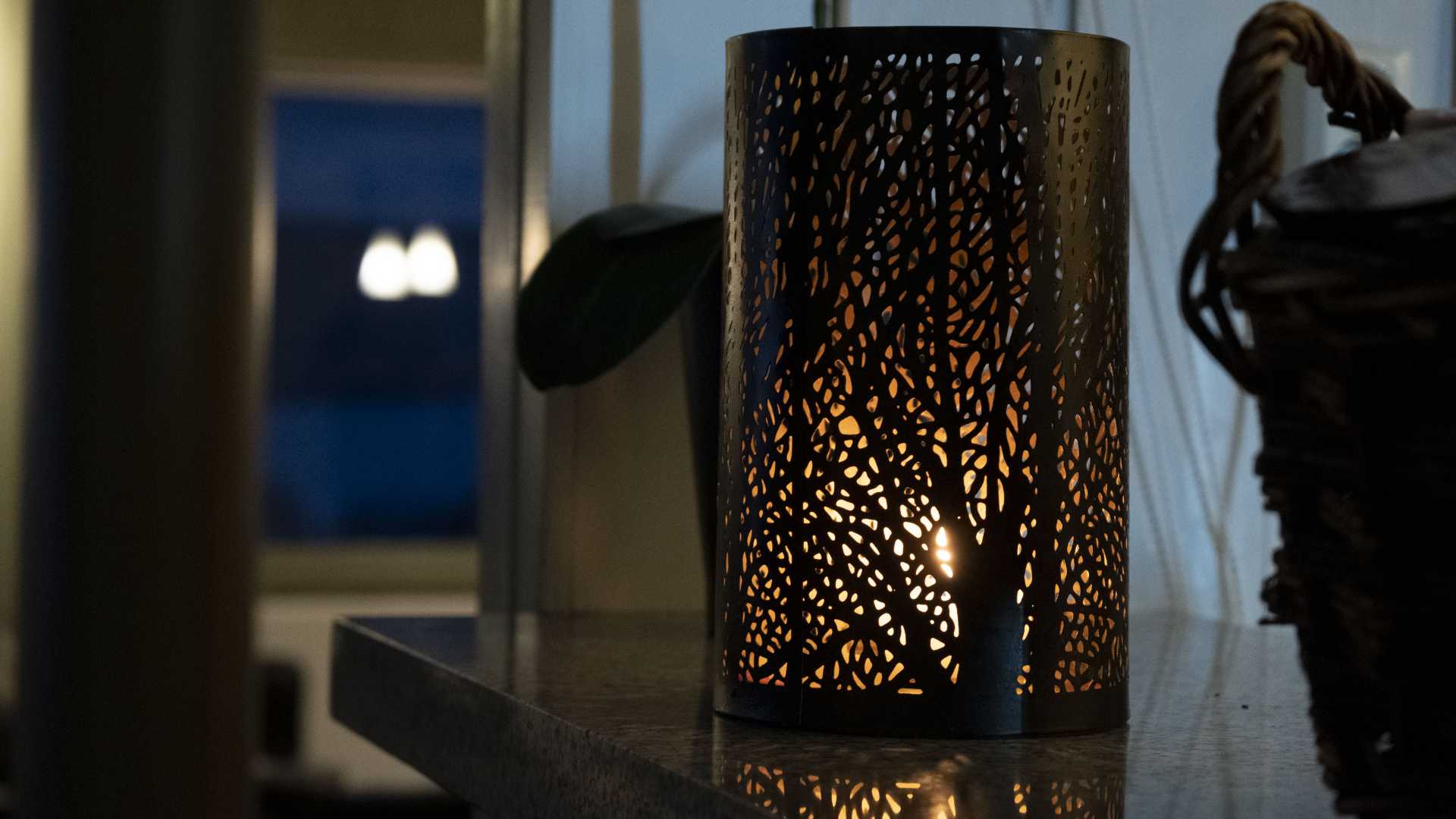 Dekorativ lysholder med utskjæringer, tent lys inni, plassert på et bord i en koselig kveldsstemning.