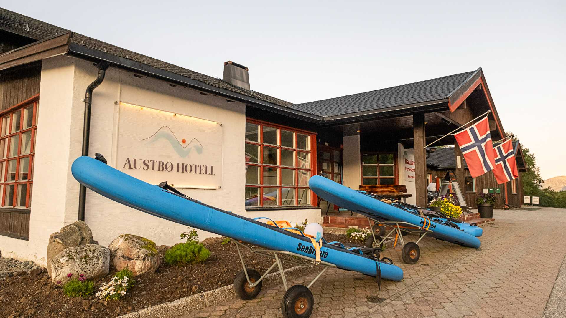 Austbø Hotell med kajakker og norske flagg foran inngangen i solnedgangen.