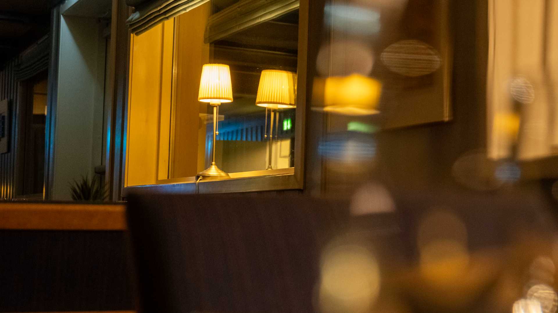 En koselig lampe reflekteres i et speil på en restaurant om kvelden, med varm belysning og stille atmosfære.
