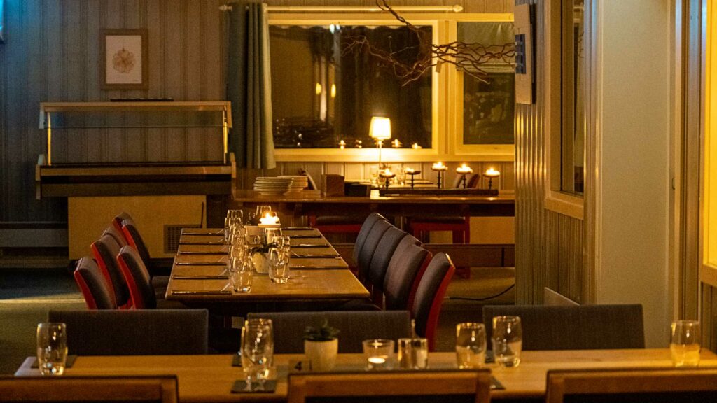 Koselig restaurantinteriør med tente lys, glass og dekkede bord i et varmt og innbydende miljø.