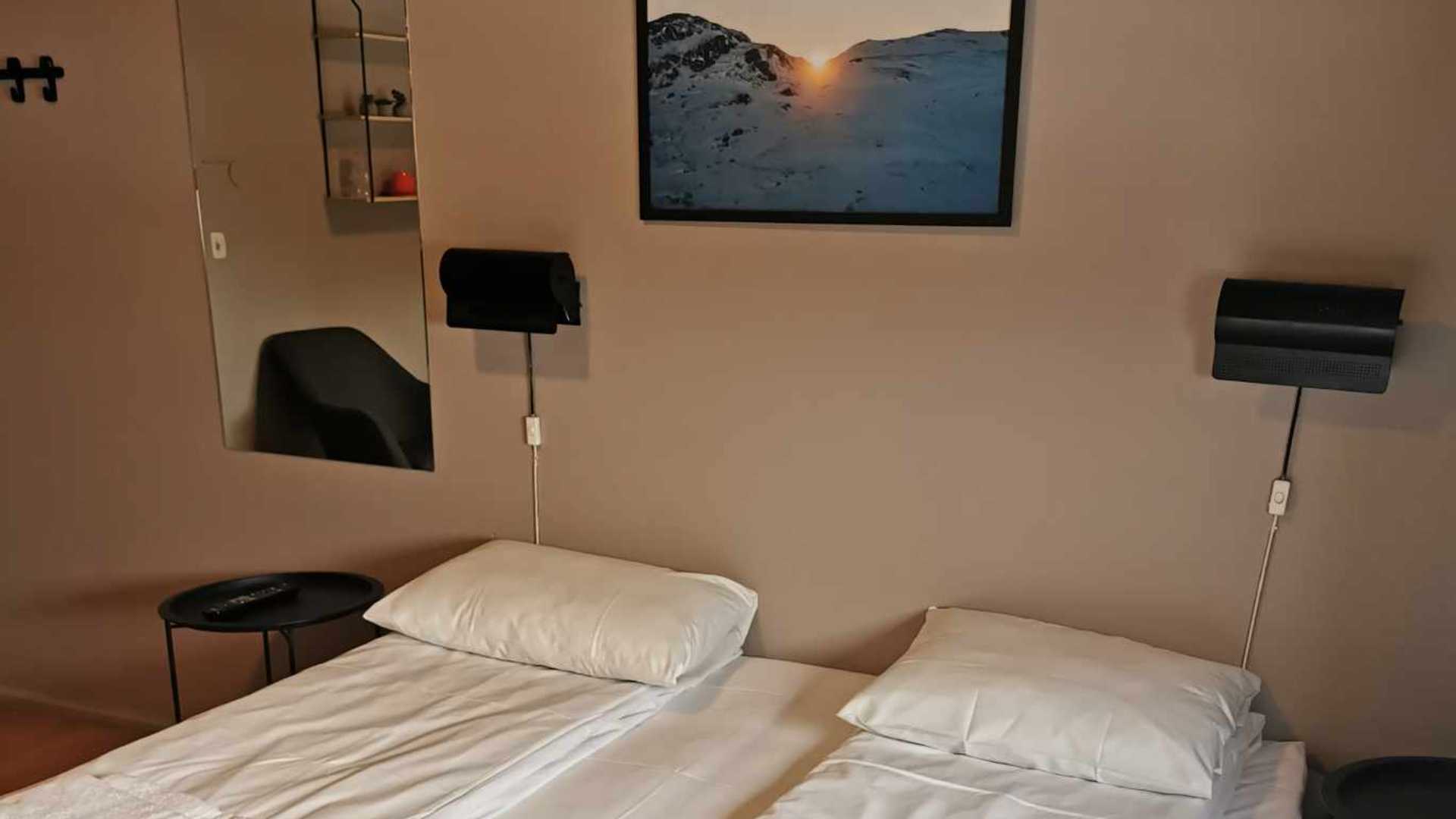 Dobbeltseng med hvitt sengetøy, vegglamper, bilde med solnedgang, dekorative hyller i et moderne soverom.