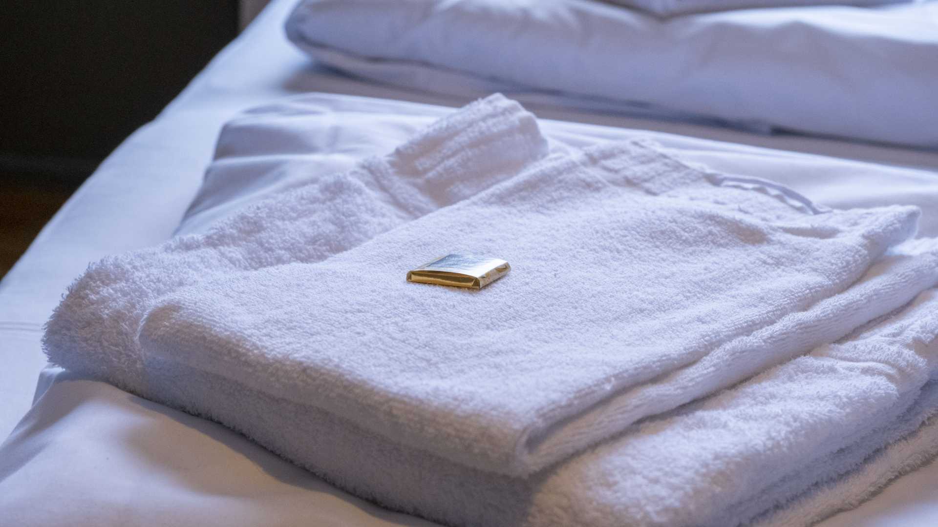 Brettet hvitt håndkle med såpestykke på seng for hotellkomfort.