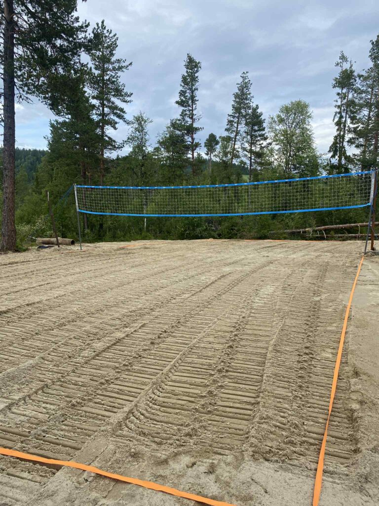 Sandbane for volleyball i skogsområde med nett i klarvær, omgitt av høye trær. Klar til kamp.