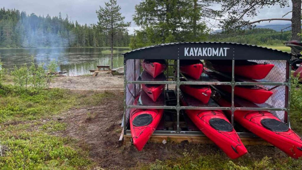Kajakker stablet ved innsjø i norsk natur med røyksky og landskap i bakgrunnen.
