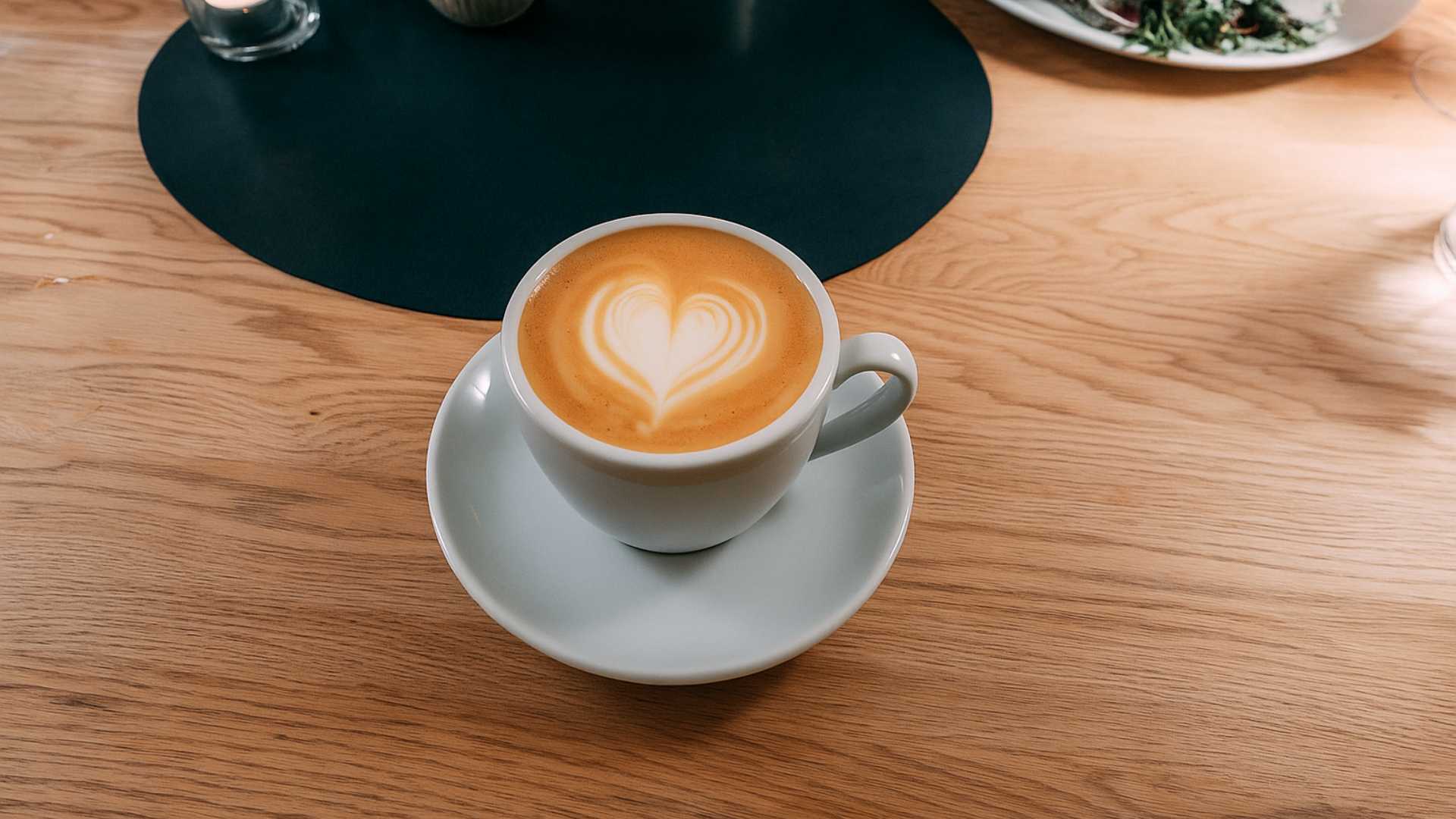 Kopp med cappuccino på trebord, hjerteskum på toppen. Perfekt for en koselig kafémorgen eller et velsmakende kafébesøk.