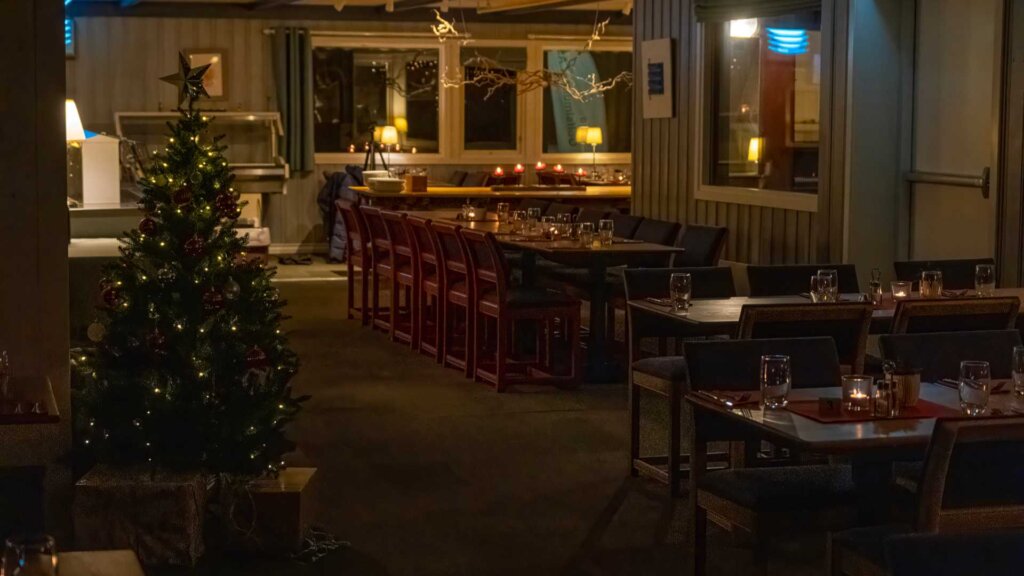 Koselig restaurant med juletre og bord lysende av stearinlys i stemningsfull belysning.