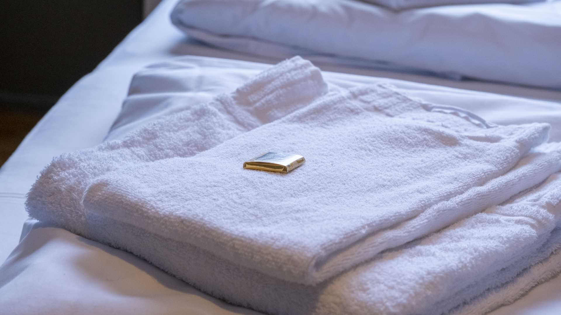 Hvit morgenkåpe med liten såpestykke på seng i et hotellrom, symbol på komfort og luksus.