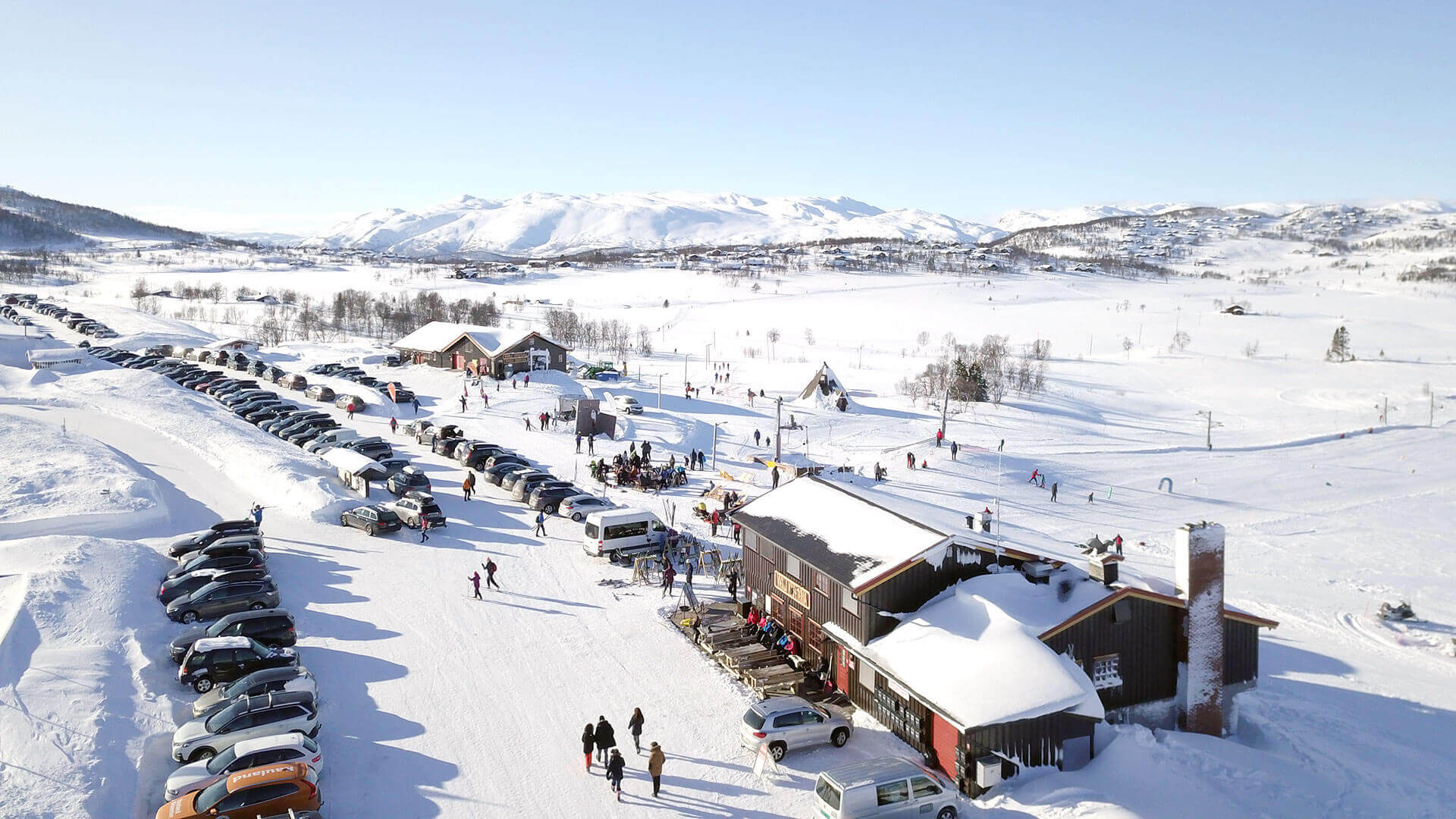 Vinteraktiviteter i norsk snølandskap med biler, hytter og folk som nyter skiturer.