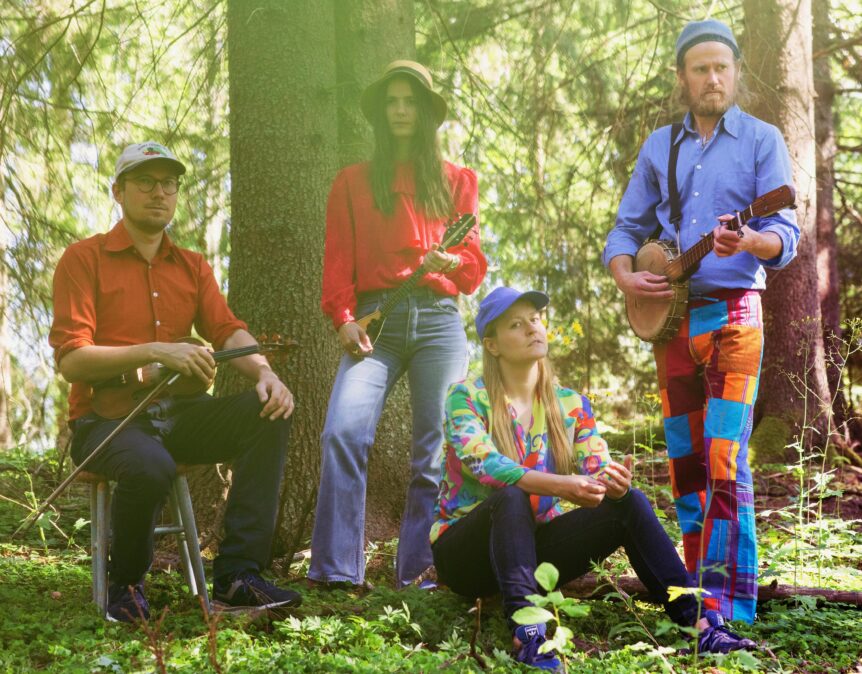 Gruppe av fire musikere med instrumenter i skogmiljø, med fargerike klær og naturlig lys.