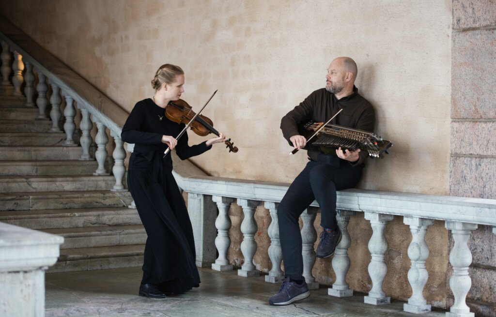 To musikere spiller fiolin og nøkkelharpe på en trapp med balustrade.