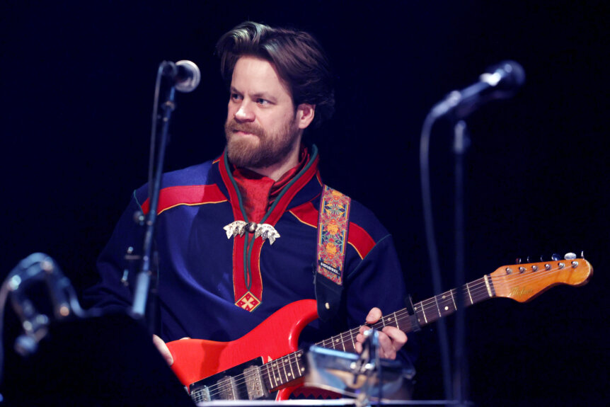 Musiker spiller elektrisk gitar i tradisjonell drakt på scenen.