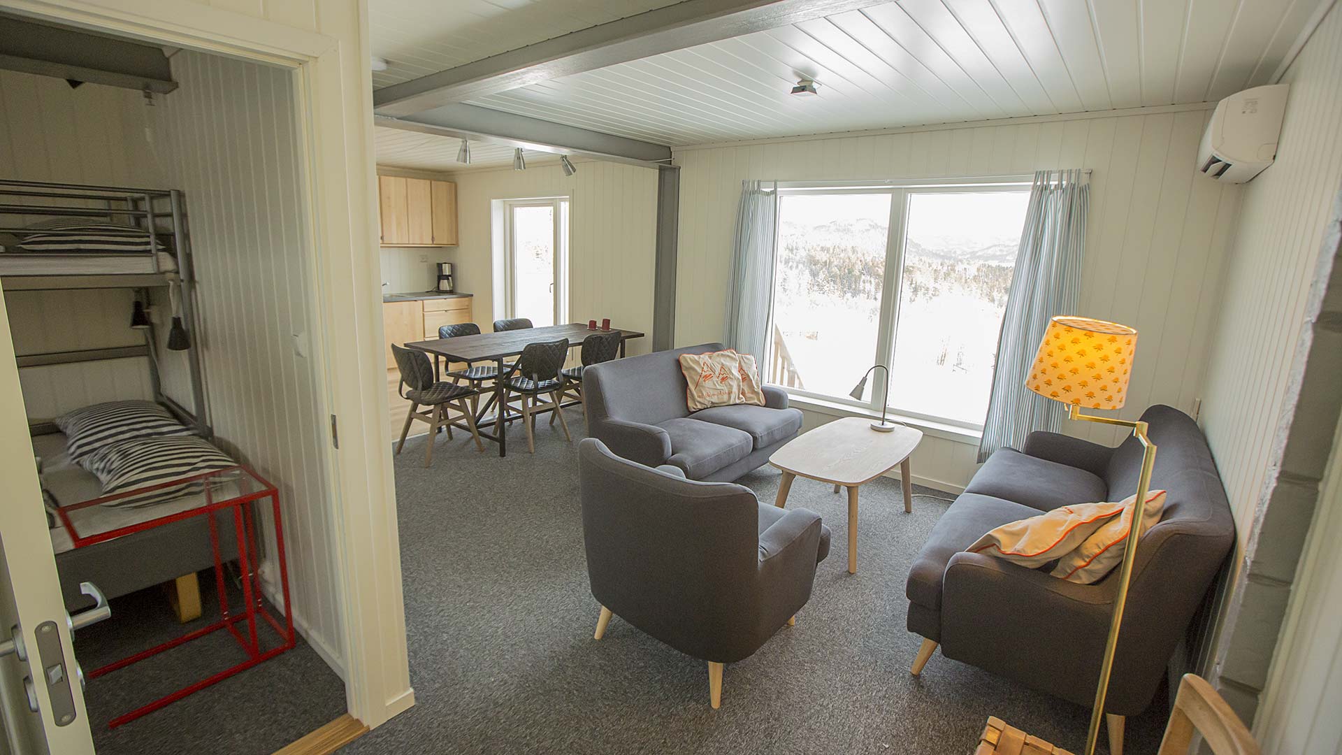 Lyst og koselig stue med sofa, spisebord og utsikt mot fjellene. Moderne interiør og store vinduer.