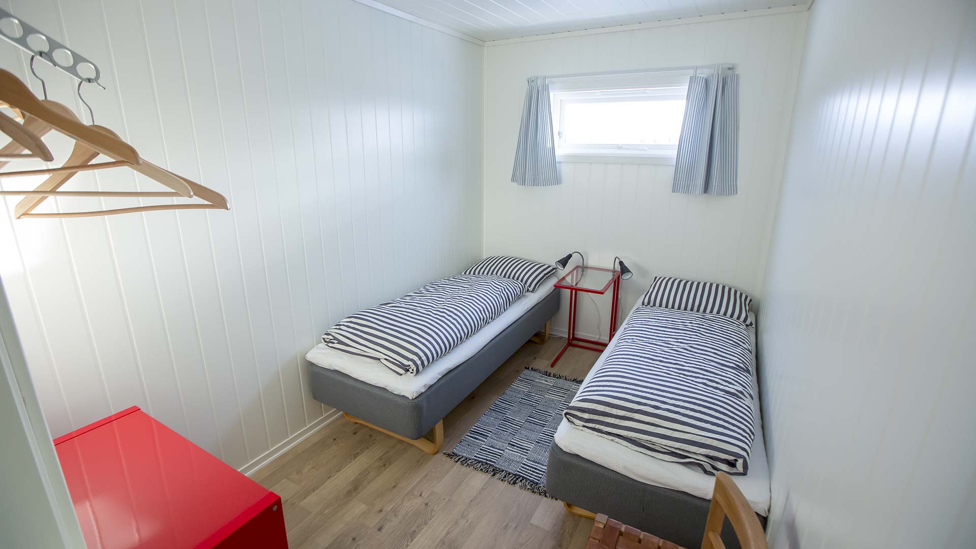 To enkeltsenger i et lyst rom med stripete sengetøy og rød kommode.