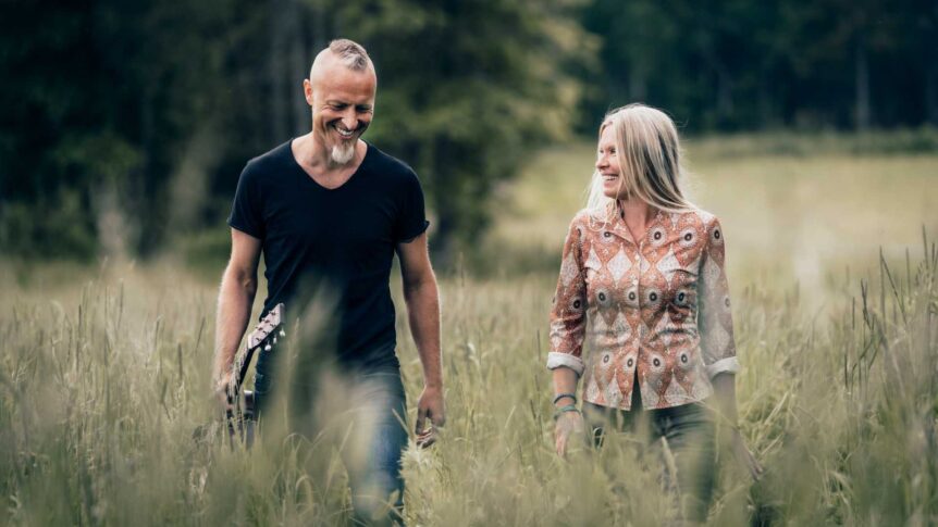 To mennesker smiler mens de går gjennom en gressdekt eng med skog i bakgrunnen.