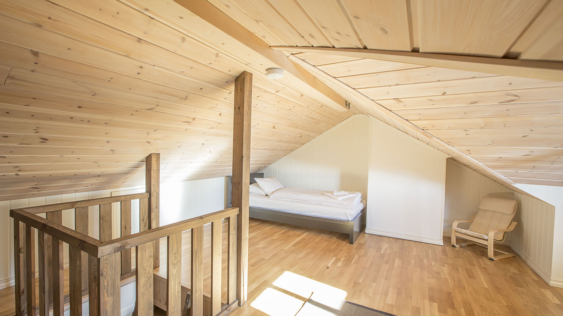 Lyst loftrom med seng, trepanel og stol, interiørdesign i skandinavisk stil.