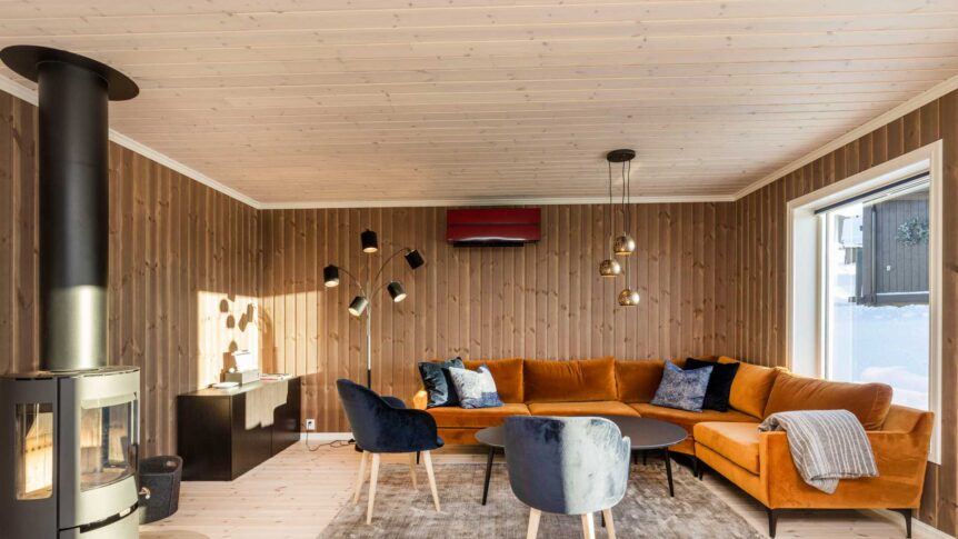 Moderne stue med oransje sofa, vedovn og store vinduer, gir komfort og stil i vinterhytteomgivelser.