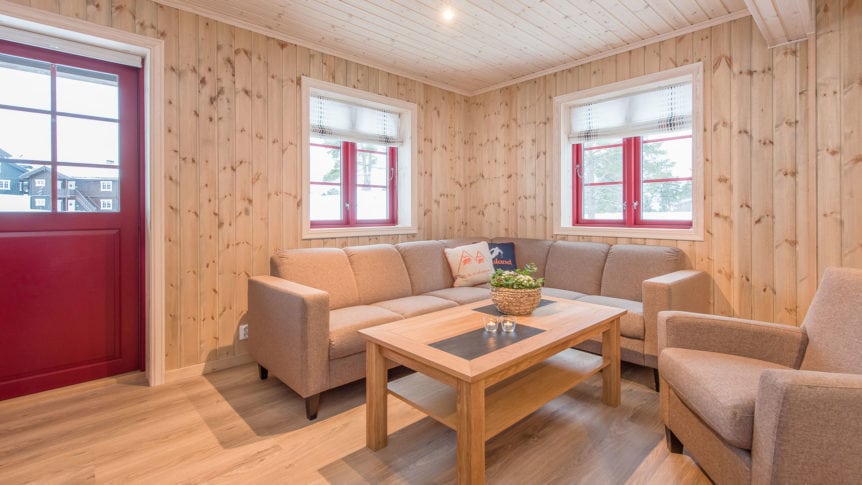 Koselig stue med trefargede vegger, beige sofa, rød dør og vindu, og trebord med dekorasjon.