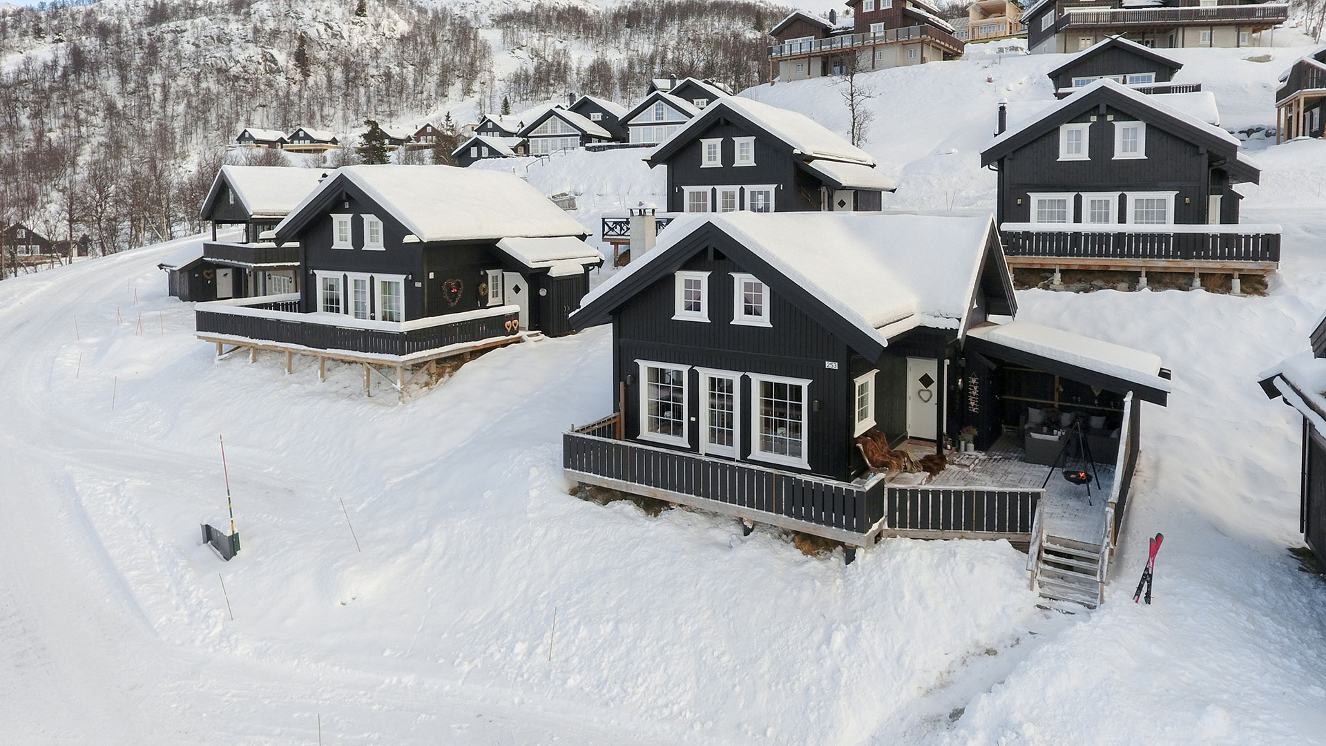 Mørke trehytter i snødekt fjellandskap i Norge, med verandaer og snødekte tak.