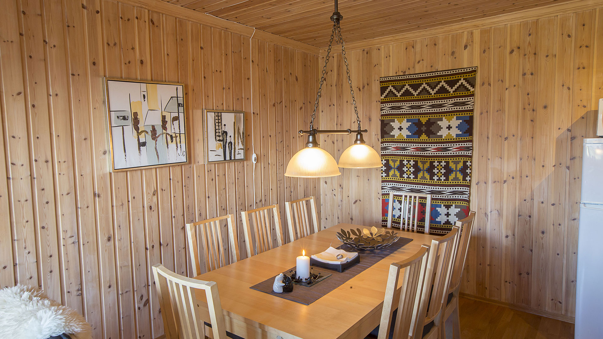 Spisestue i tre med seks stoler, lysestake og kunstverk på veggen, opplyst av to hengelamper.