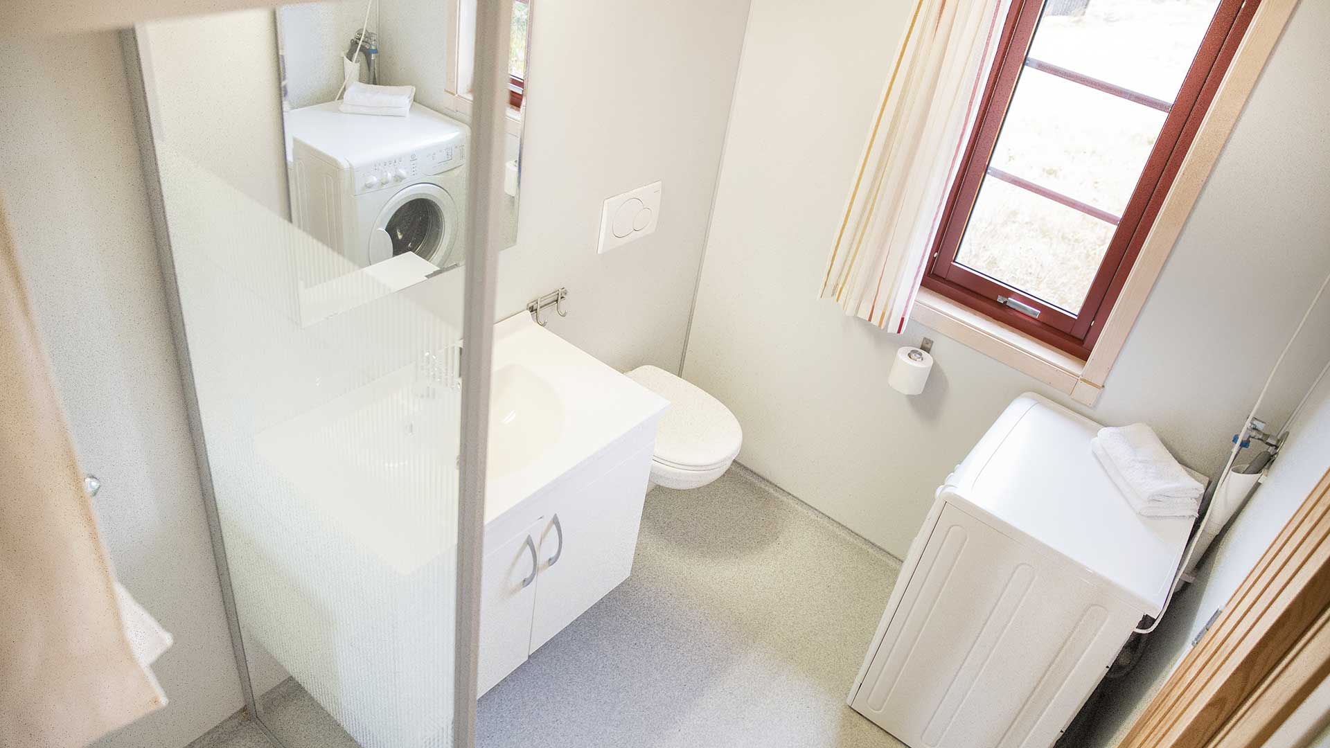 Moderne baderom med vaskemaskin, dusj, toalett og vindu. Lyst interiør og rent design i et lite rom.