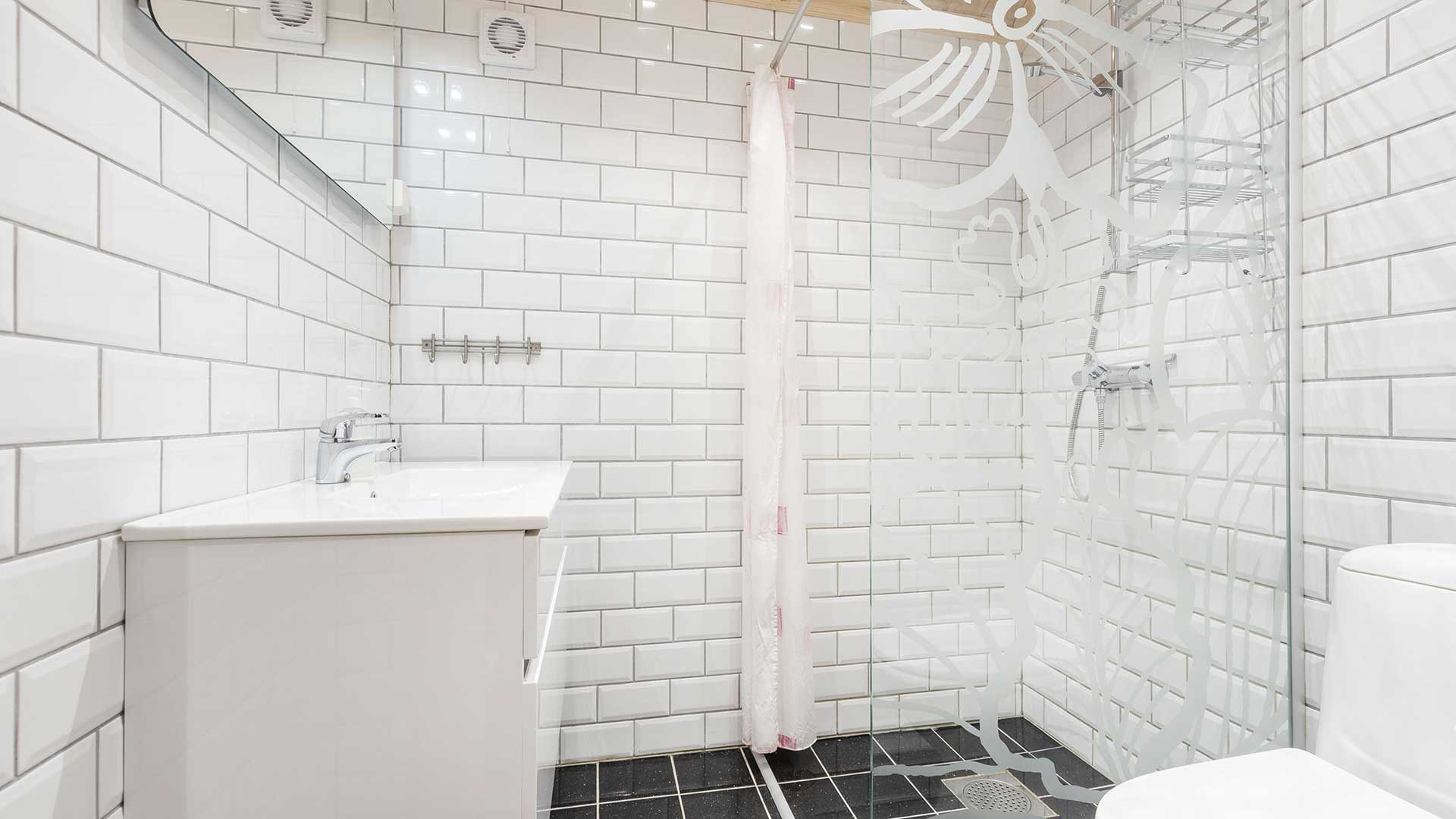 Moderne, lyst bad med hvite fliser, dusjkabinett i glass og svart gulvflis, minimalistisk design.