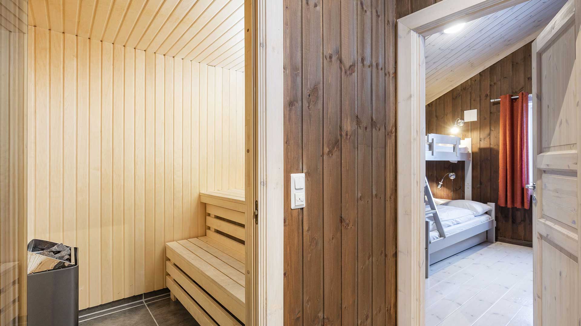 Innsiden av en moderne badstue med tilstøtende soverom med køyeseng og røde gardiner. Skandinaviskt interiørdesign.
