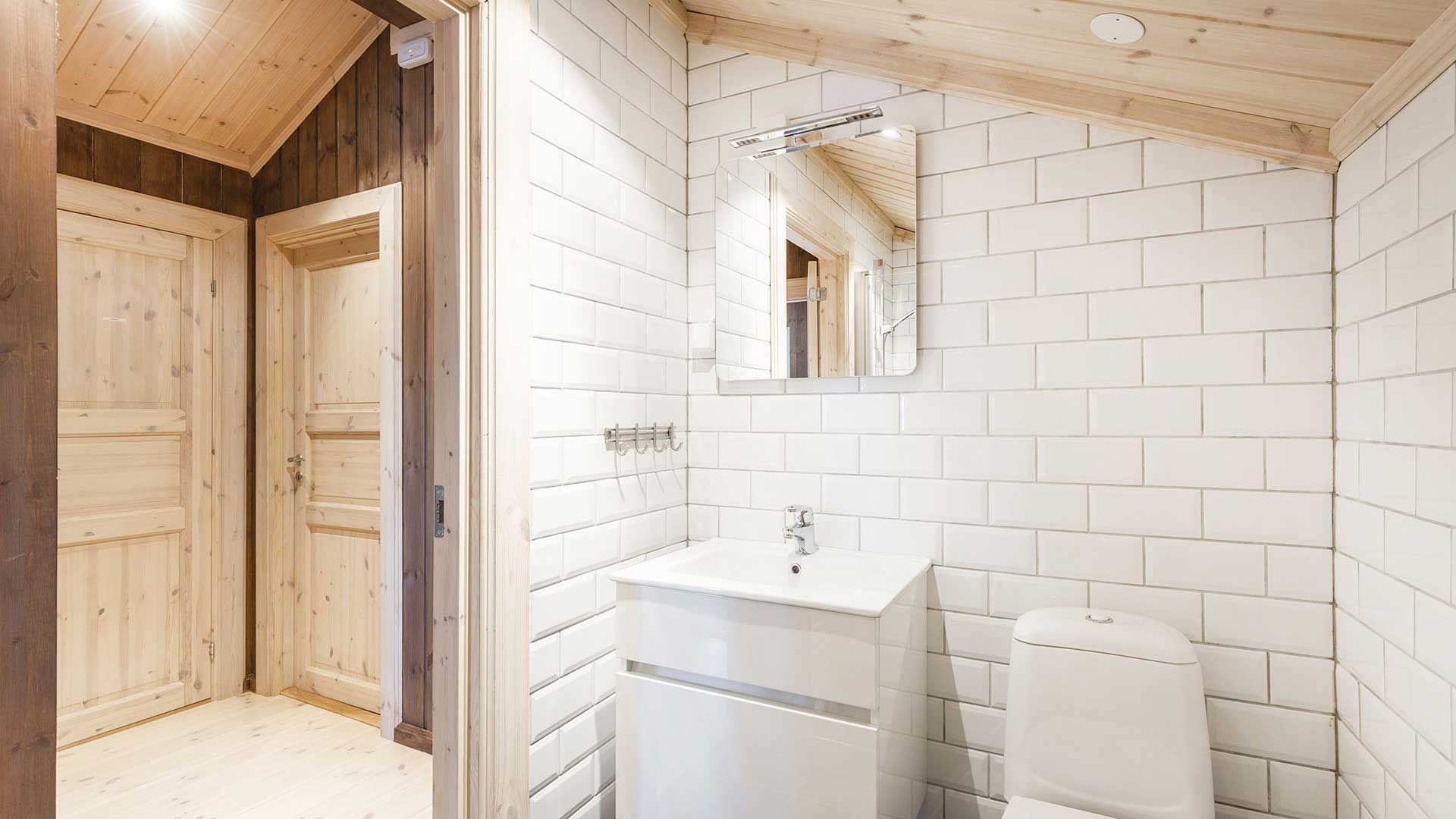 Moderne bad med hvite fliser og trepanel. Inneholder servant med speil og toalett. Skandinavisk design.