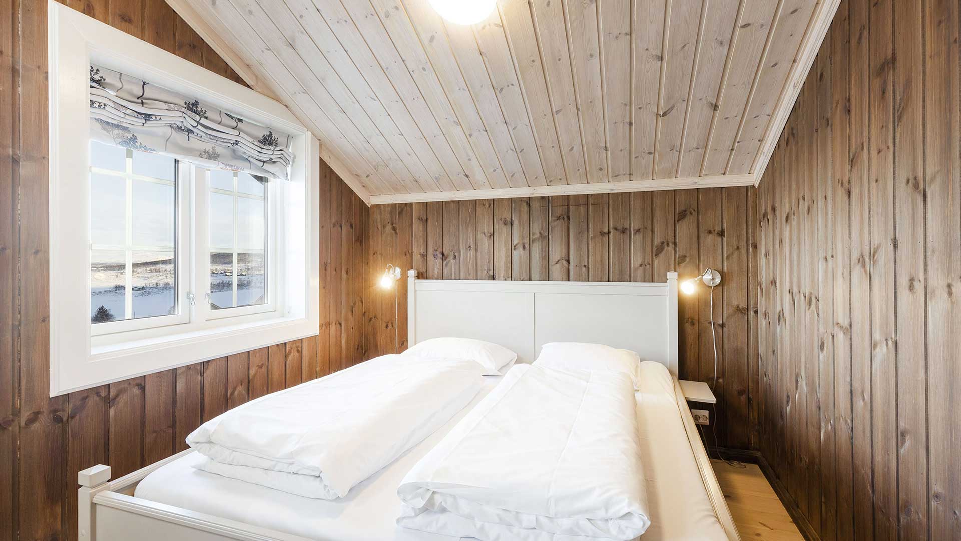 Koselig soverom med hvit dobbeltseng og utsikt mot snødekt landskap gjennom vinduet.
