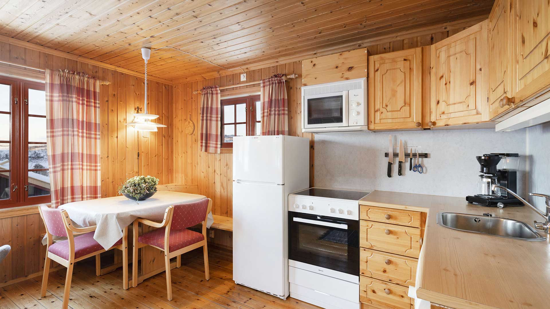 Koselig kjøkken i hytte med treverk, spiseplass, hvitevarer og utsikt mot snødekte fjell.