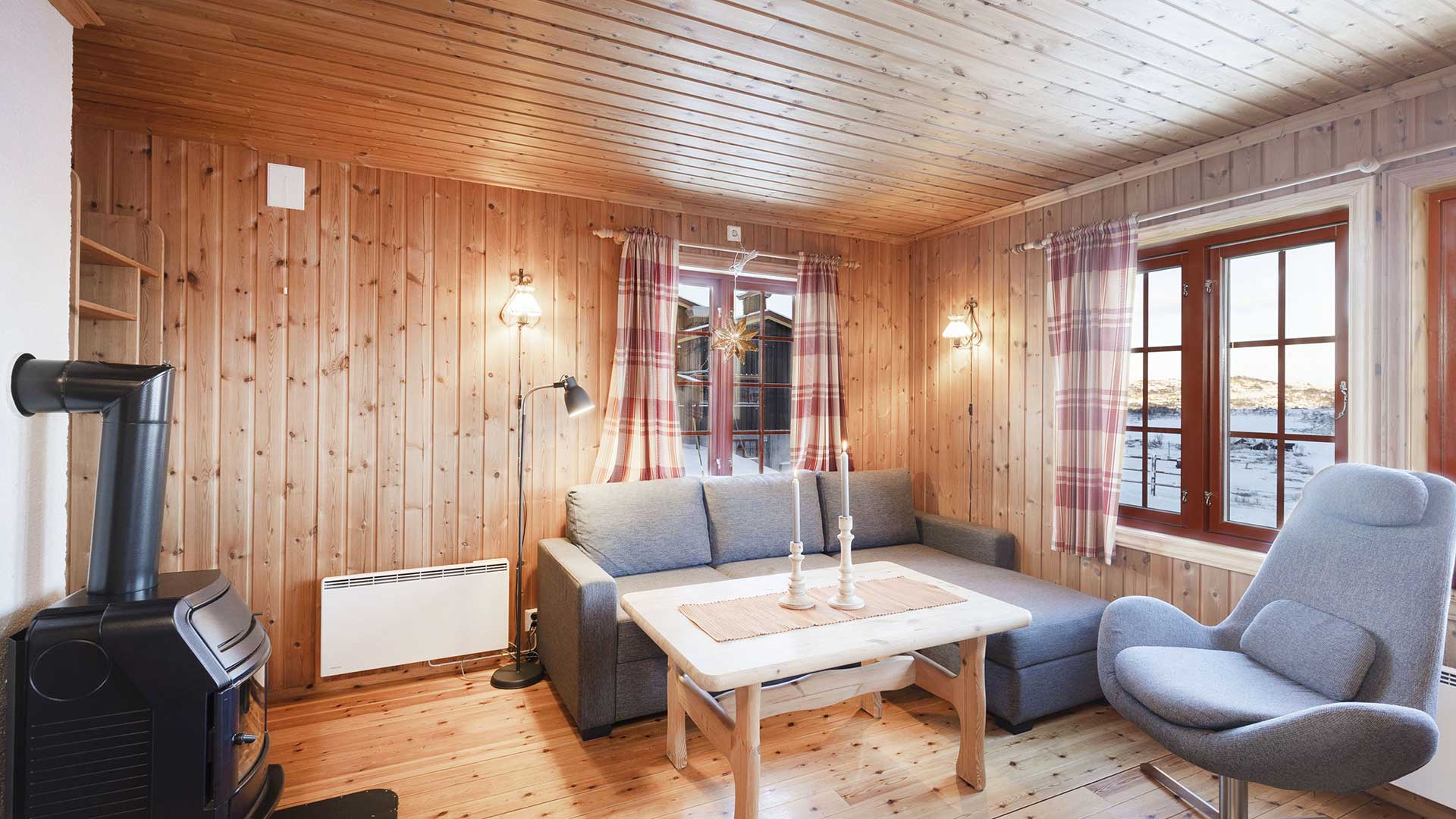 Koselig norsk stue med trevegger, peis, sofa og utsikt. Behagelig atmosfære med klassisk skandinavisk interiør.