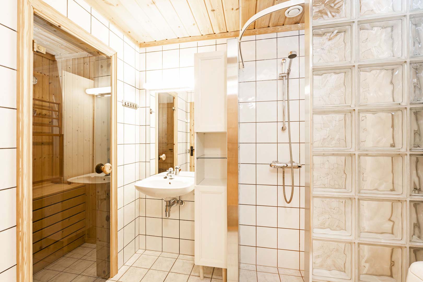 Lyst flislagt bad med dusj og sauna, moderne design og glassdetaljer for en luksuriøs følelse.