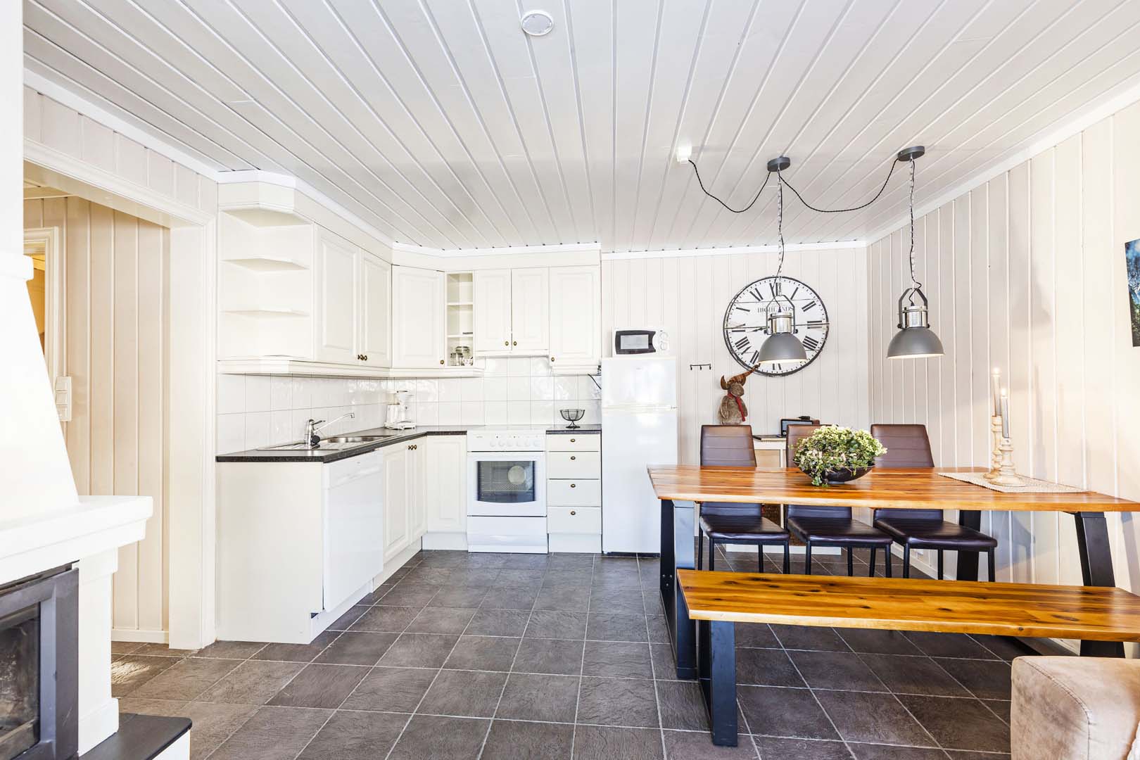 Moderne hvitt kjøkken med rustikk spisestue, klokke og hengende lamper. Stilfullt interiør.