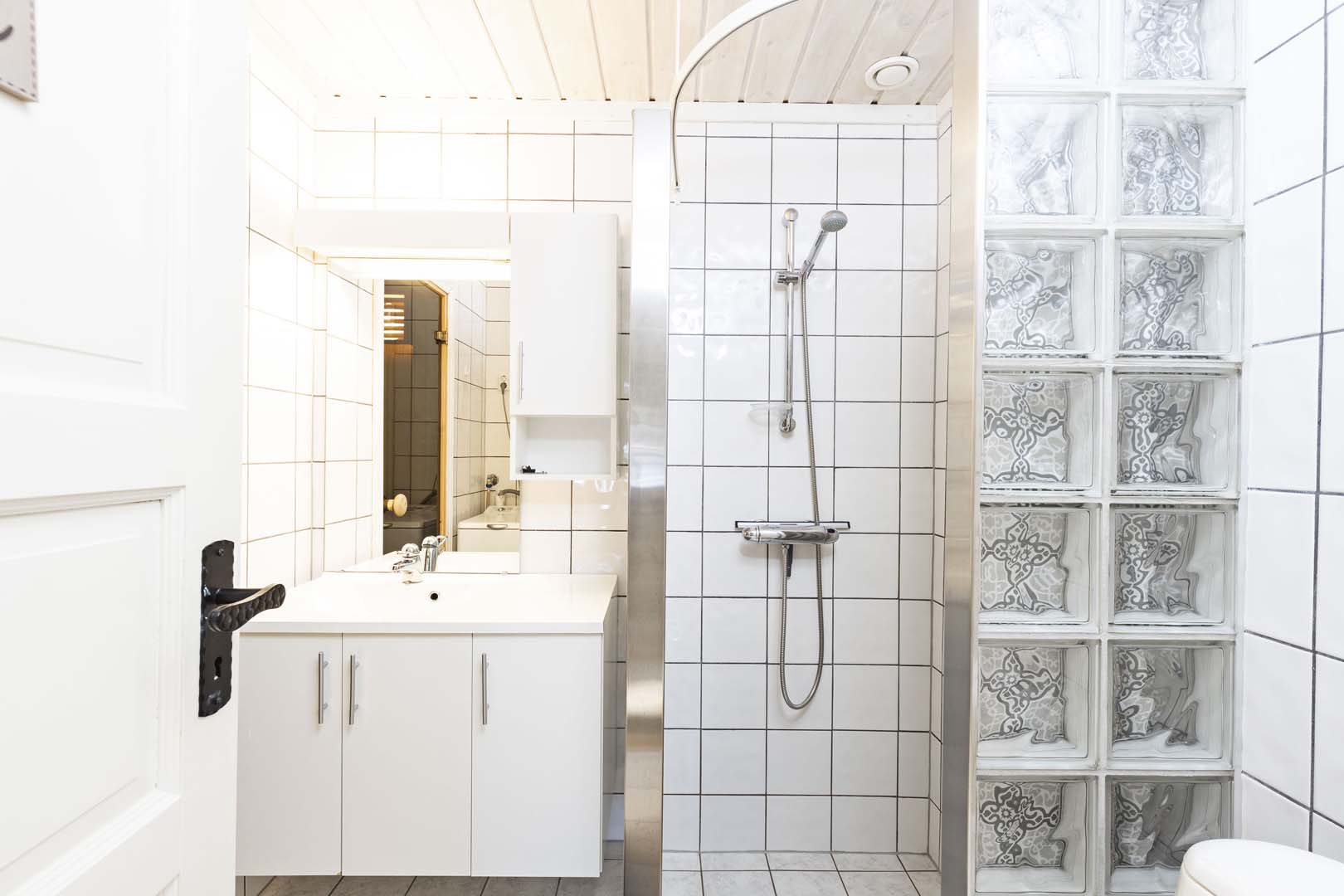Lyst og moderne bad med dusjhjørne, hvite fliser og minimalistisk innredning.