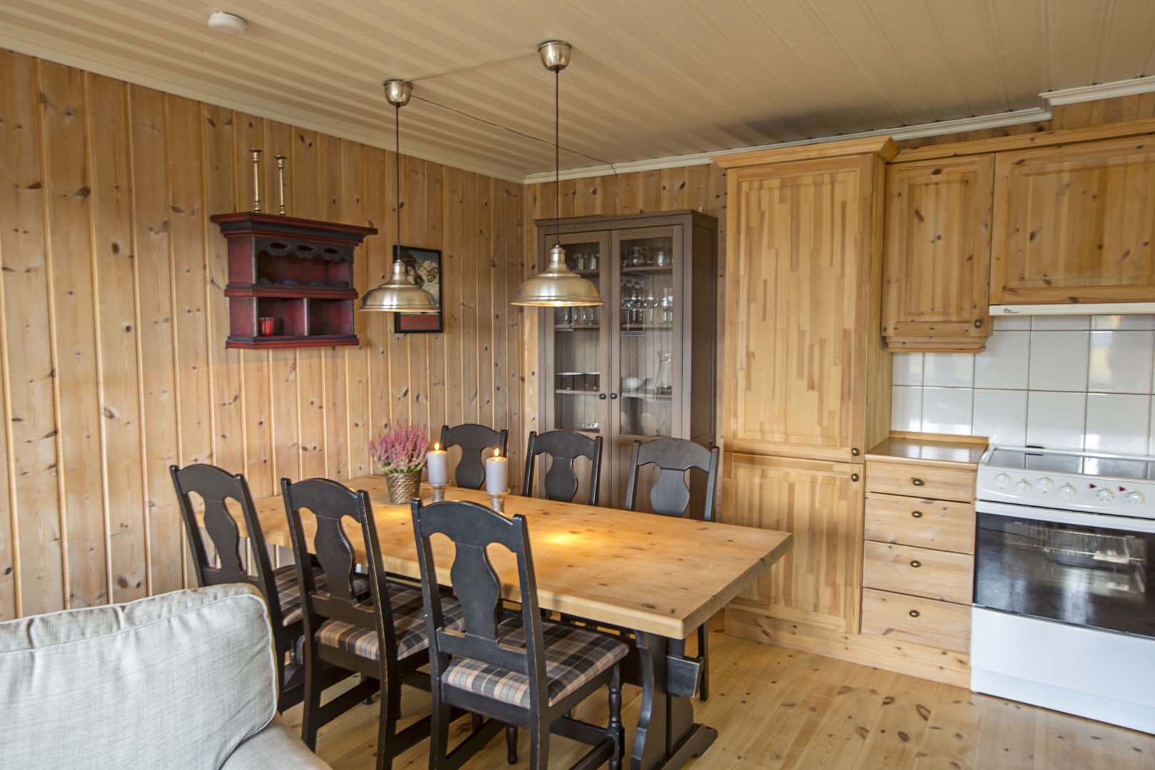 Koselig spisestue med trepanel, spisebord og stearinlys. Perfekt for hyggelige måltider i norsk hyttestil.