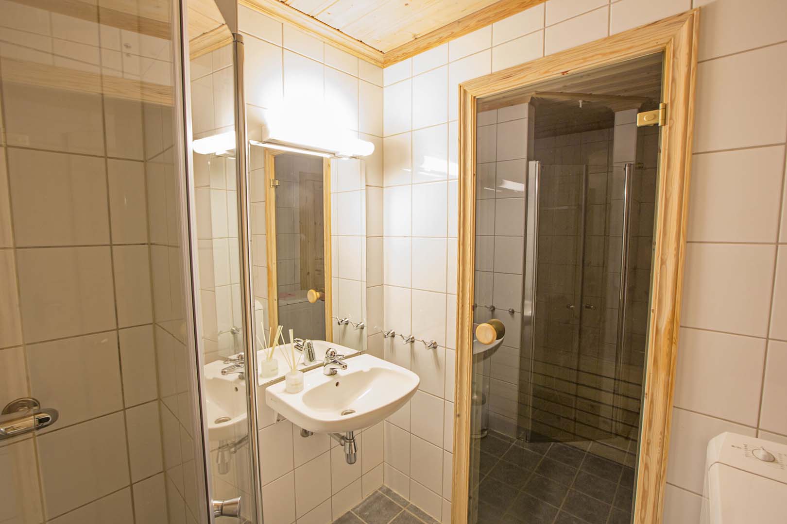 Moderne bad med hvite fliser, speilskap og dusjkabinett.