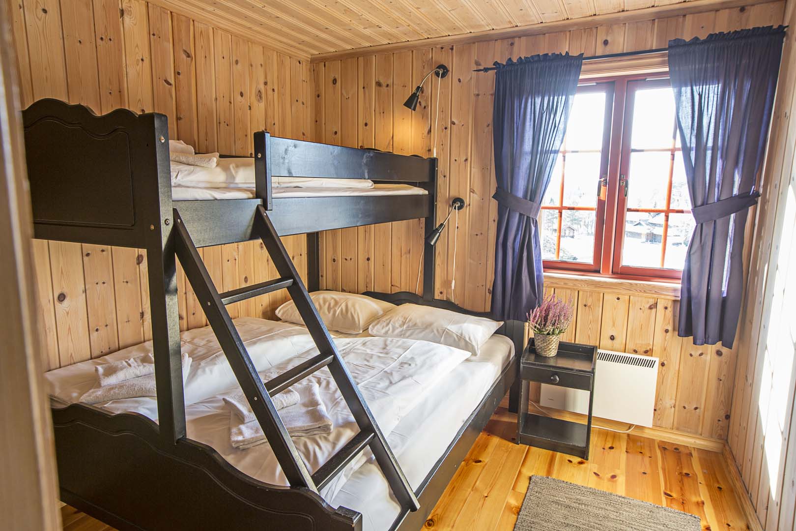 Koselig soverom med køyeseng i trepanel, vindu med utsikt, lilla gardiner og dekorert nattbord.