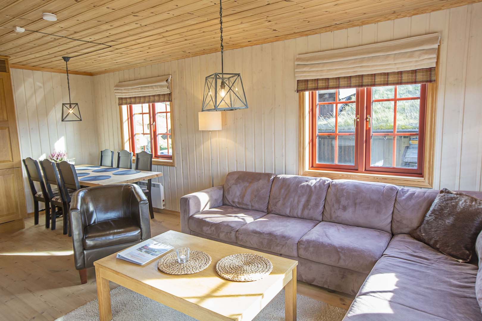 Koselig stue med sofa, spisestue og store vinduer, innredet i tre for en varm og innbydende atmosfære.