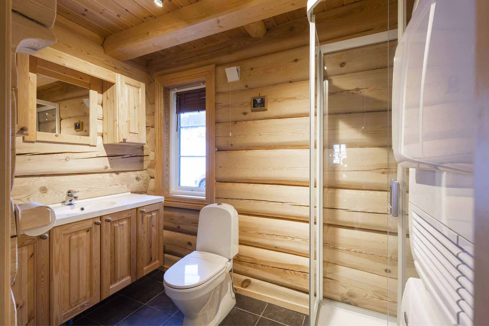 Bad i trepanel med dusjkabinett, toalett og vask. Naturlig lys fra vindu gir varm atmosfære.