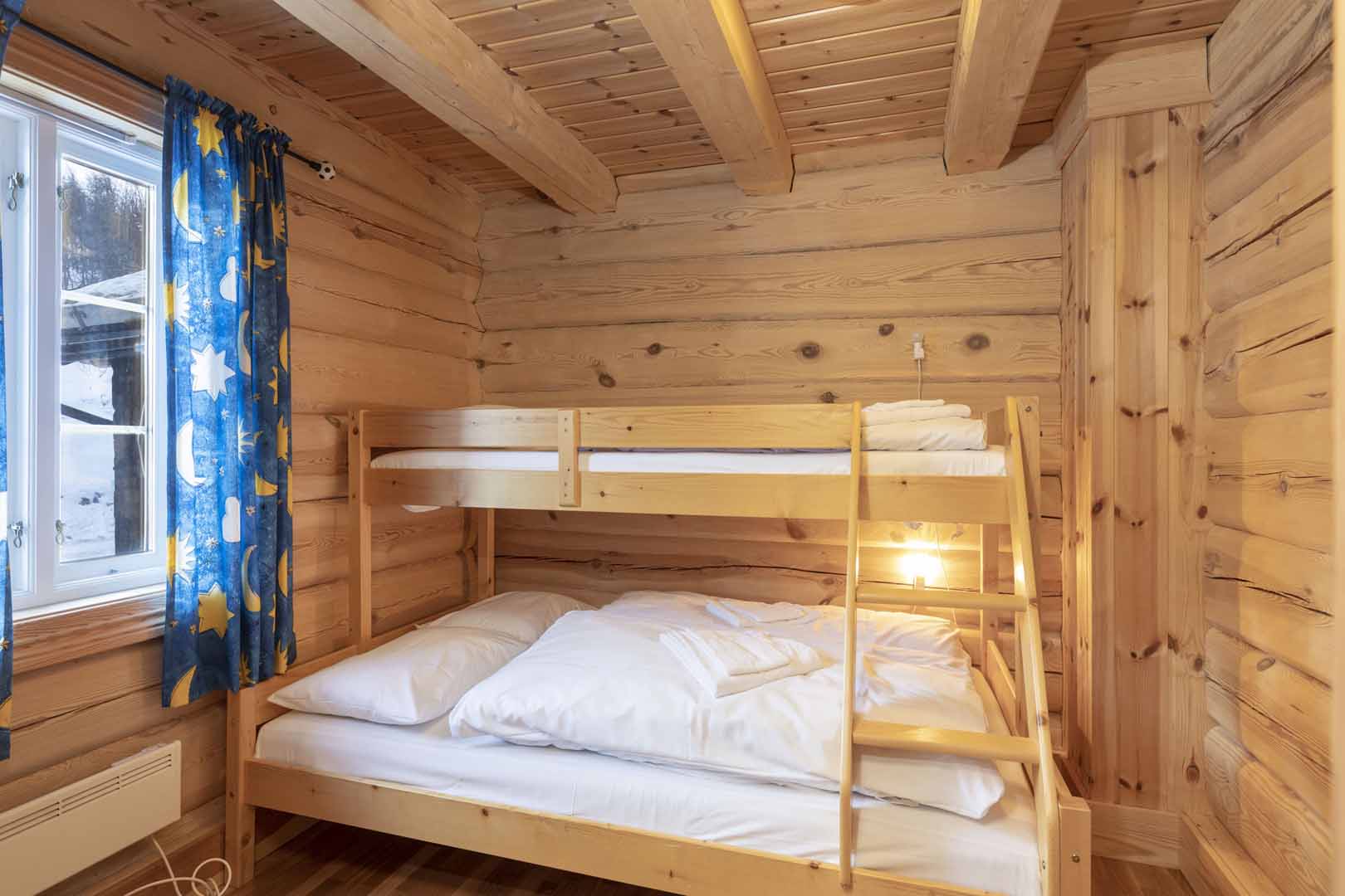 Koselig tømmerhytte med køyeseng, blå gardiner og naturlig treinteriør. Perfekt for vinterovernatting.