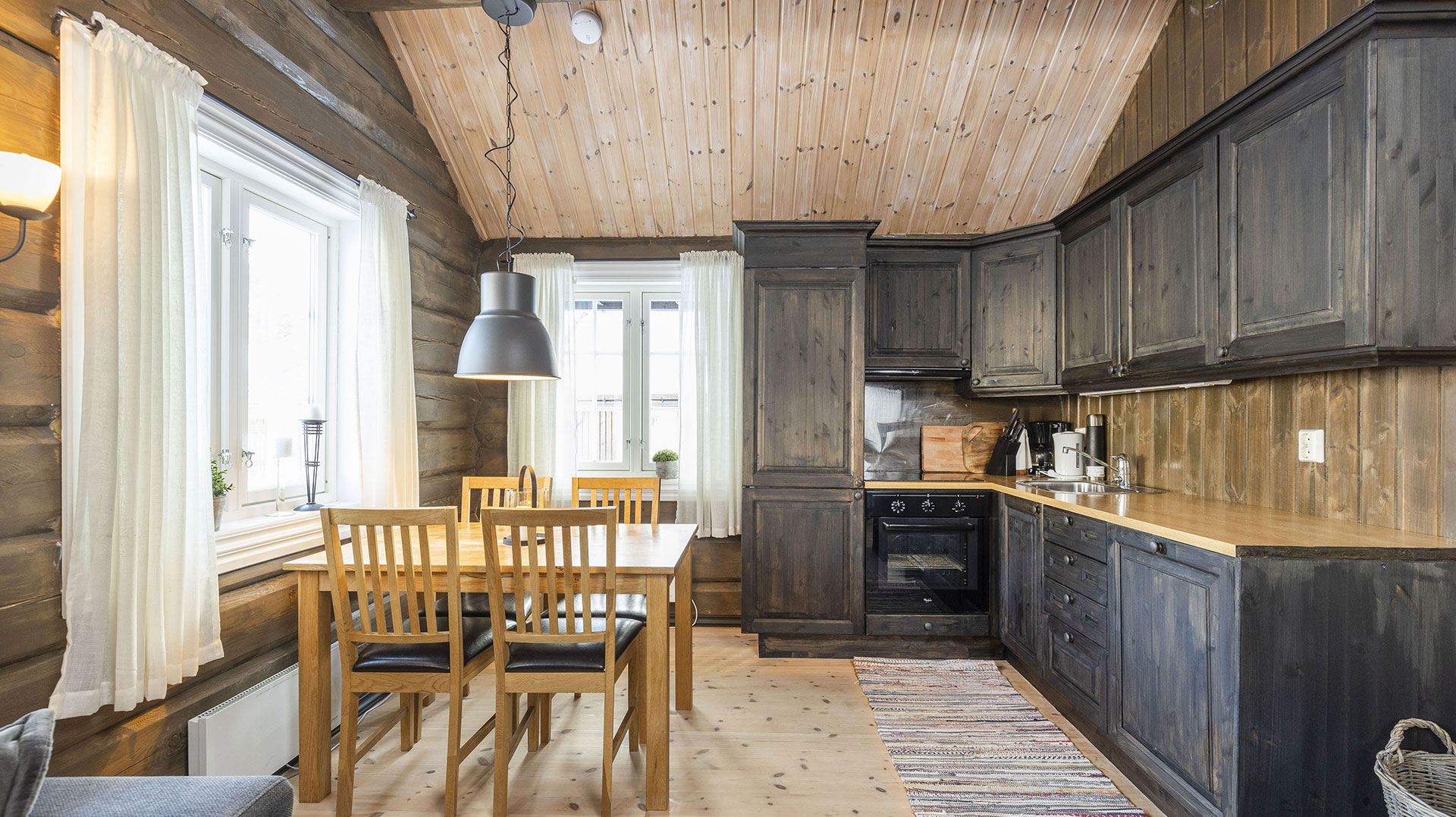 Koselig kjøkken i trehytte-stil med spisebord, mørke skap og lyse vinduer. Perfekt for fjellhytter.