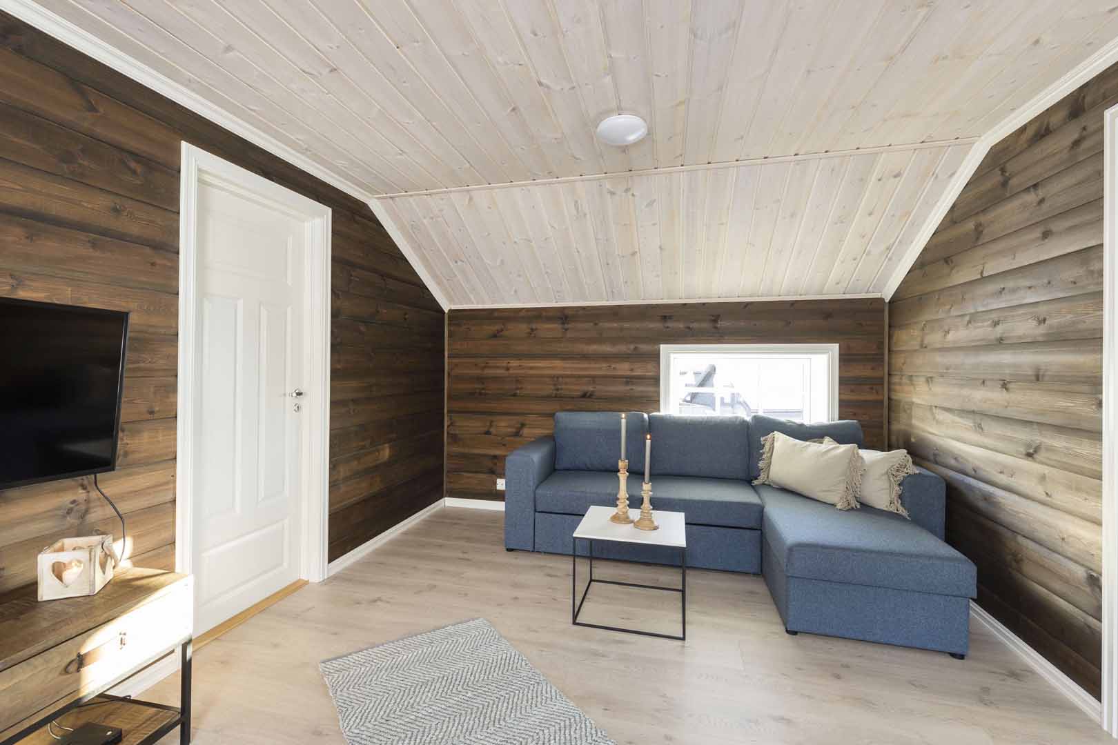 Stue med blå sofa, hvite panelvegger og TV, skandinavisk stil. Koselig interiørdesign for hjemmet.