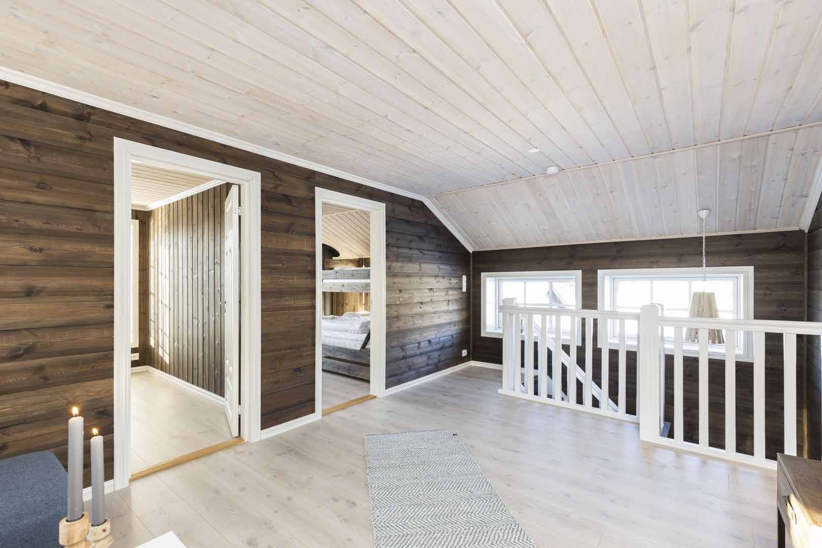 Lyst og luftig loftsrom med tregulv, hvite detaljer og synlige bjelker. To åpne dører, utsikt til soverom med køyeseng.