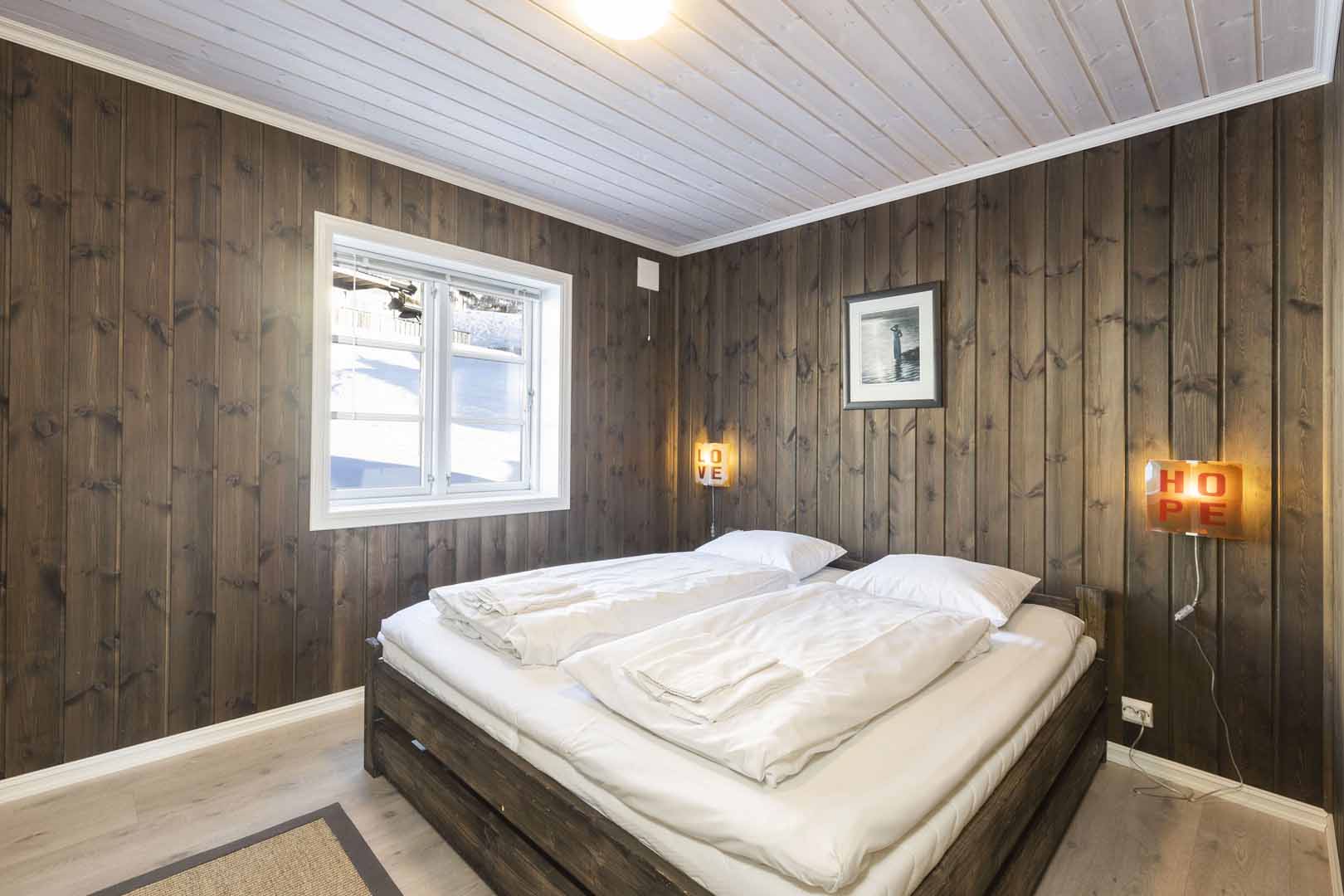 Koselig soverom i treverk med dobbelseng og vindu, dekorert med skilt som sier LOVE og HOPE.
