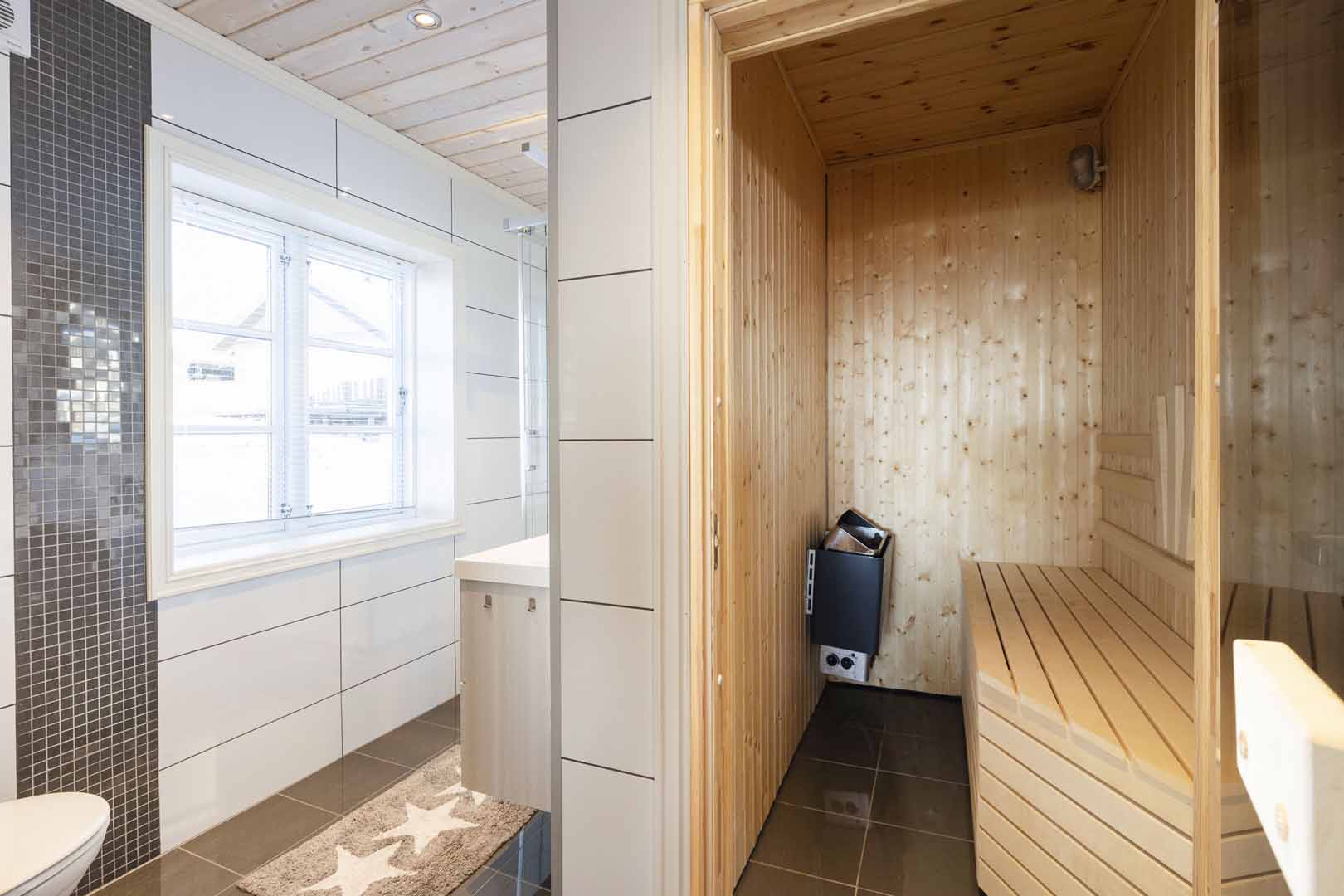 Moderne baderom med tilstøtende badstue, flislagt gulv og lyst interiør.