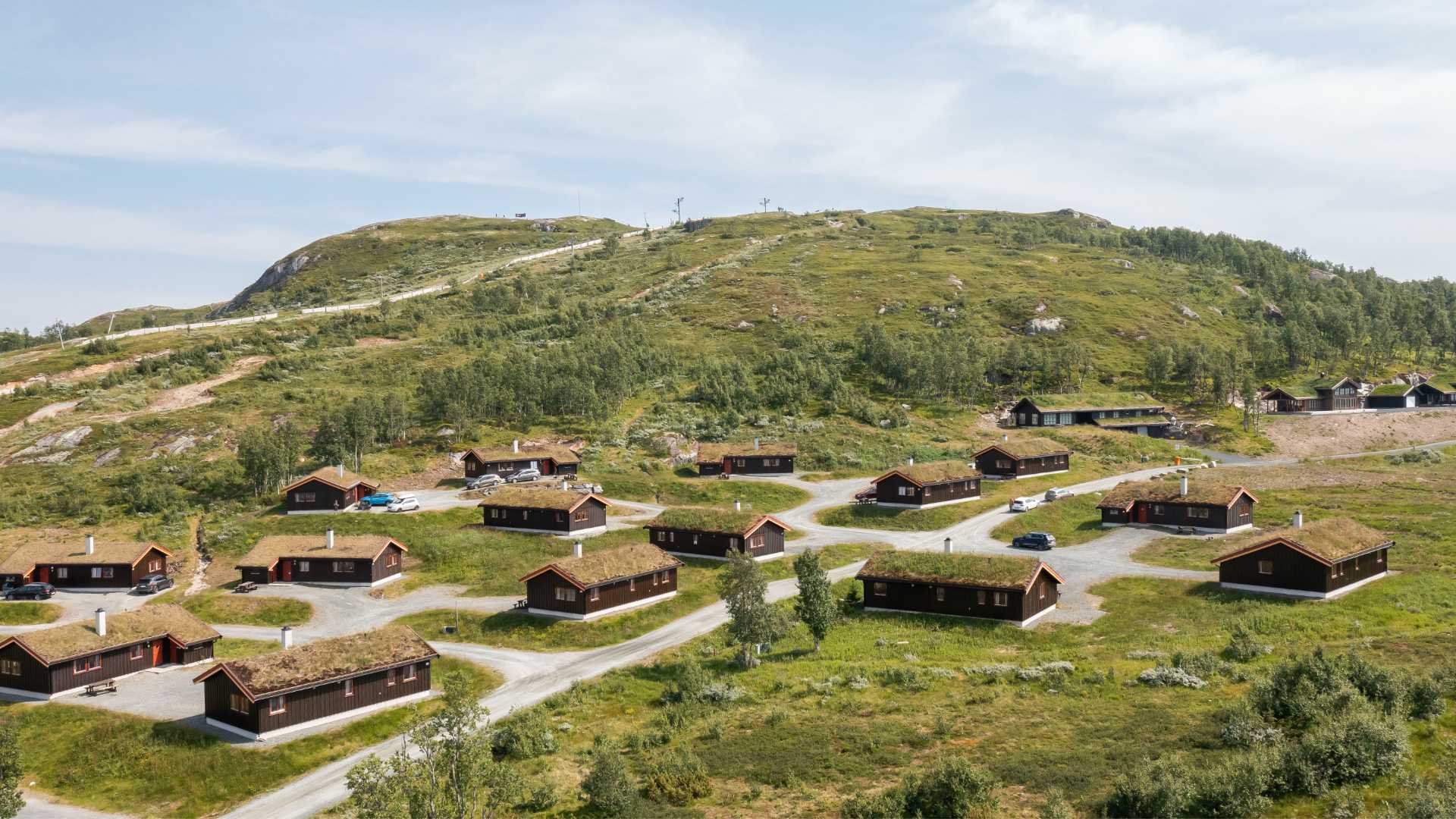 Fjelldal med norske hytter og torvtak omringet av grønne bakker under en klar himmel.